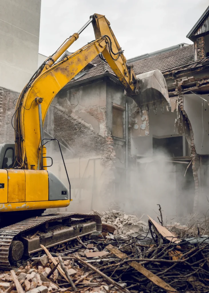 Pelle de démolition jaune qui abat la façade d’une maison ancienne pendant des travaux de démolition de maison